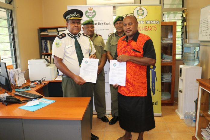 Commissioner Gabriel Manelusi and Dr. Paul Orotaloa smiling with the signing document
